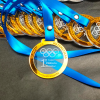 Primer plano de una medalla de acrílico doble capa personalizada con borde espejo dorado, con una escala de medallas desenfocada en el fondo para mostrar volumen.