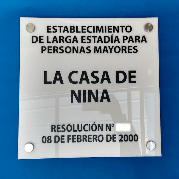 Vista frontal de letrero ELEAM en acrílico blanco de 5mm con gráfica normativa negra y fijaciones metálicas.